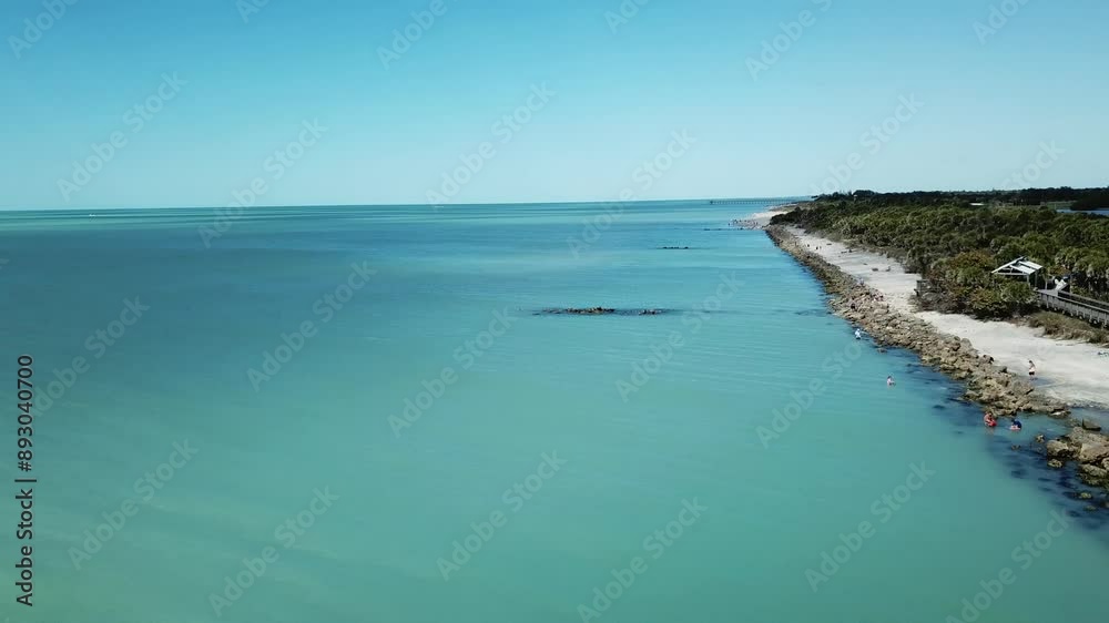 Aerial view of a rocky shoreline extending into a calm blue sea, with beachgoers and a wooden walkway. Aerial view of a rocky shoreline extending into a calm blue sea, with beachgoers and a wooden walkway.