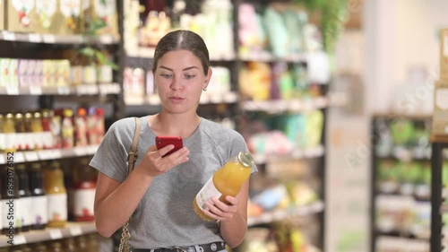 Young woman in supermarket scan QR code bottle of drink. Girl buyer photo information on packaging of bio product.  photo