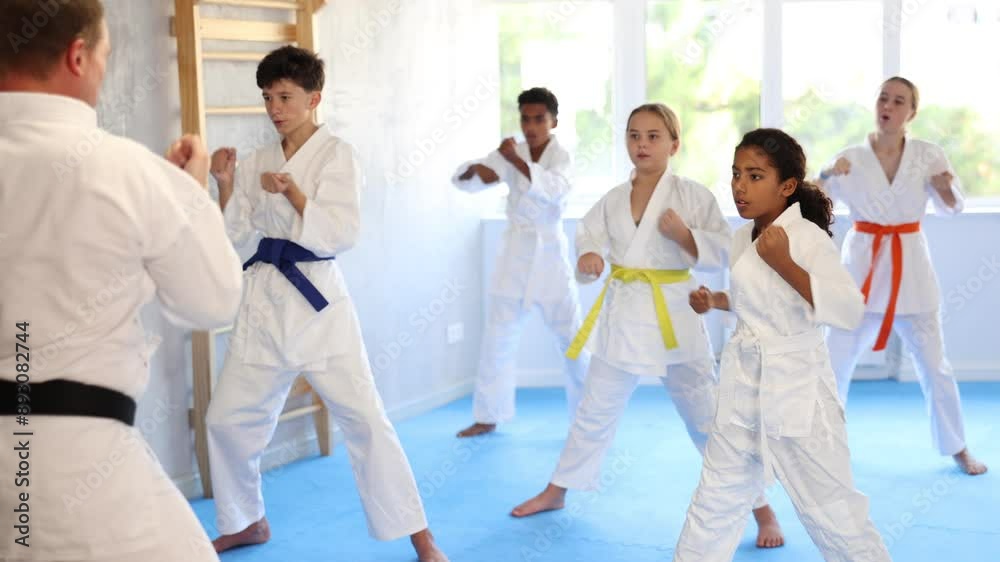 Motivated sporty black girl with group of tweens wearing white kimonos diligently performing kata routines to hone karate techniques in training room. High quality 4k footage