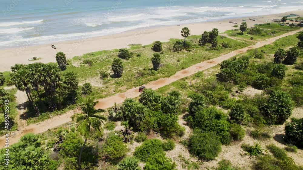 Red tuk-tuk driving along a coastal dirt road through lush green scenery, aerial view Red tuk-tuk driving along a coastal dirt road through lush green scenery, aerial view