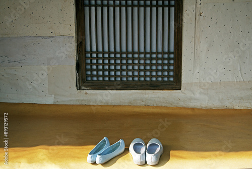 Suncheon-si, South Korea - November 25, 2010: Front view of a couple's white rubber shoes in front of window door of a thatched house at Naganeupseong Folk village
 photo