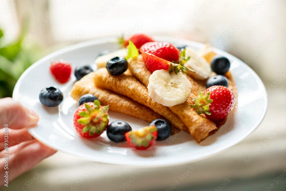 A man's hand holds a plate of delicious and appetizing pancakes with berries. A man's hand holds a plate of delicious and appetizing pancakes with berries.