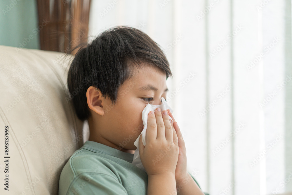 Young asian boy sneezing or blowing his nose and mouth with tissue, cold allergies or illness, health, virus and flu season, RSV, Influenza, childcare and hygiene practices, especially for children Young asian boy sneezing or blowing his nose and mouth with tissue, cold allergies or illness, health, virus and flu season, RSV, Influenza, childcare and hygiene practices, especially for children