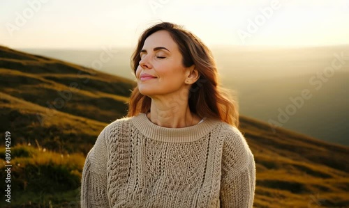 Medium shot portrait video of a woman in her 40s practicing mindfulness sophrology relaxation & stress-reduction wearing a cozy sweater against a hillside or rolling hills background