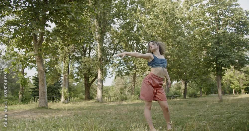 A curly-haired girl performs modern dance in a lush green park surrounded by tall trees, blending energetic movement with the beauty of nature. A curly-haired girl performs modern dance in a lush green park surrounded by tall trees, blending energetic movement with the beauty of nature.