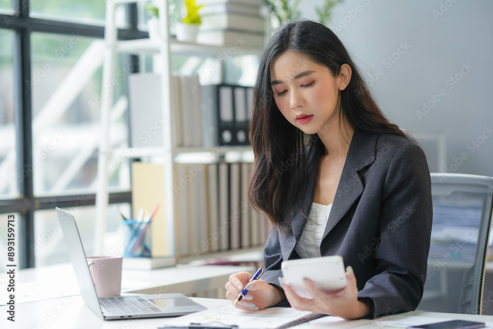 Focused young businesswoman in a modern office, using a calculator and jotting notes for a financial report. This image captures the essence of office life for a millennial entrepreneur Focused young businesswoman in a modern office, using a calculator and jotting notes for a financial report. This image captures the essence of office life for a millennial entrepreneur