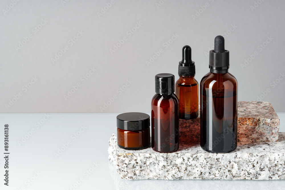 Set of brown glass bottles with essential oils on stand on gray background