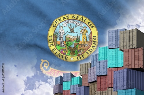 Idaho US state flag and big stack of shipping cargo containers in docks with sky background close up photo