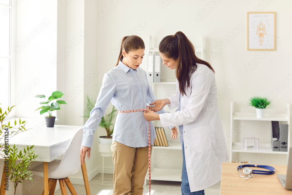 Fototapeta premium Doctor, nurse measuring young female patient waist line with tape during check up in clinic, medical exam for weight loss healthy dietary, regular medical physical examination, overall body health 