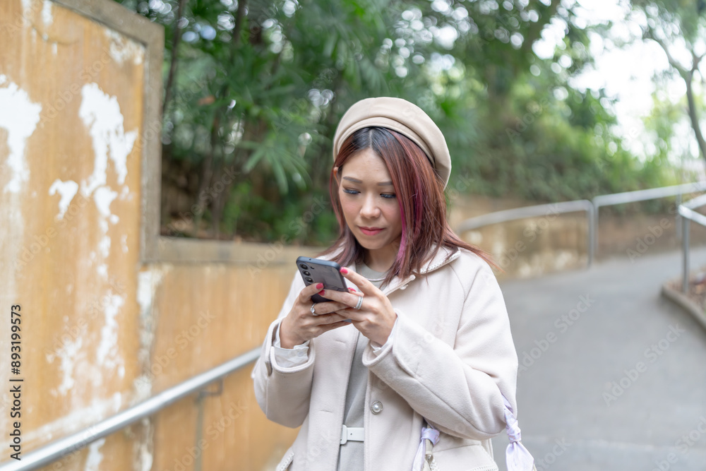 Fototapeta premium Thirty-something Hong Kong woman with reddish-brown hair using her smartphone in Kowloon Park, Tsim Sha Tsui, Kowloon Island, Hong Kong.