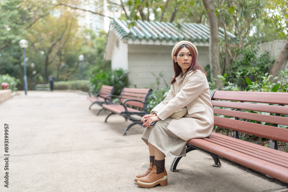 Thirty-something Hong Kong woman with reddish-brown hair sitting on a bench by a large fountain in Kowloon Park, Tsim Sha Tsui, Kowloon Island, Hong Kong, during a cold winter. Thirty-something Hong Kong woman with reddish-brown hair sitting on a bench by a large fountain in Kowloon Park, Tsim Sha Tsui, Kowloon Island, Hong Kong, during a cold winter.