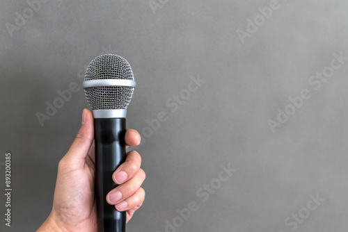 Hand holding a microphone against a plain background, representing public speaking, music, presentations, and communication concepts. photo