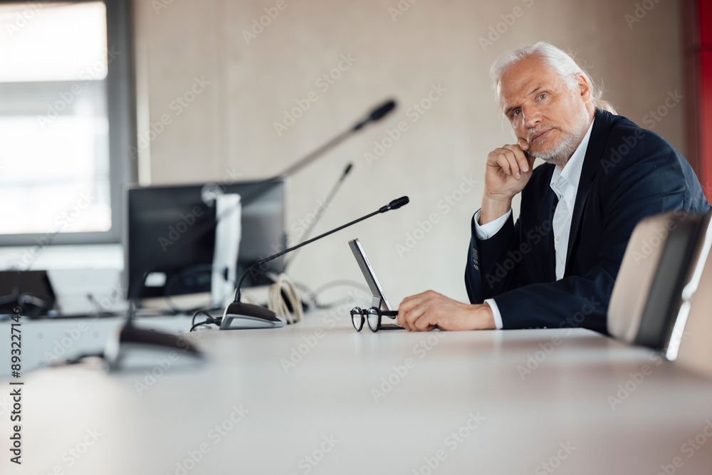 Confident senior businessman sitting at conference table in board room Confident senior businessman sitting at conference table in board room