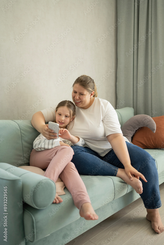 Mother using smart phone with daughter sitting on sofa at home Mother using smart phone with daughter sitting on sofa at home
