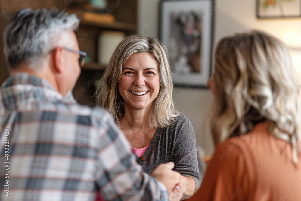Middle-aged woman smiling while shaking hands with a couple at home. Trust-building, client relations, first impressions, personal connection, social interaction. Middle-aged woman smiling while shaking hands with a couple at home. Trust-building, client relations, first impressions, personal connection, social interaction.