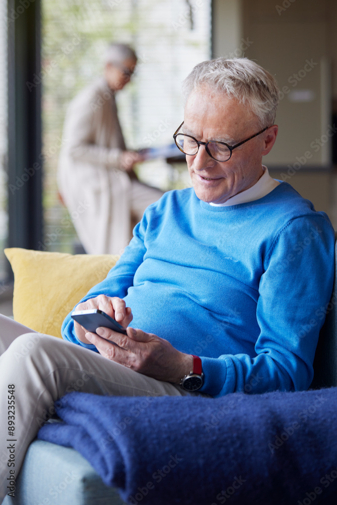 Senior man sitting on couch at home using mobile phone Senior man sitting on couch at home using mobile phone
