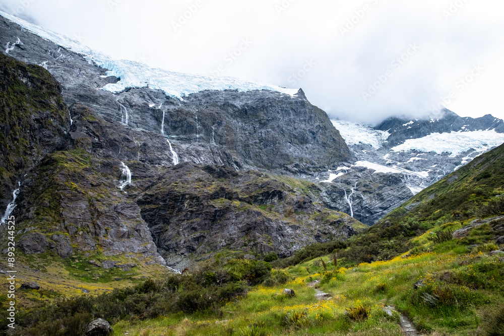 A stunning view of a glacier with multiple waterfalls cascading down the rugged mountain, surrounded by vibrant green meadows. A stunning view of a glacier with multiple waterfalls cascading down the rugged mountain, surrounded by vibrant green meadows.