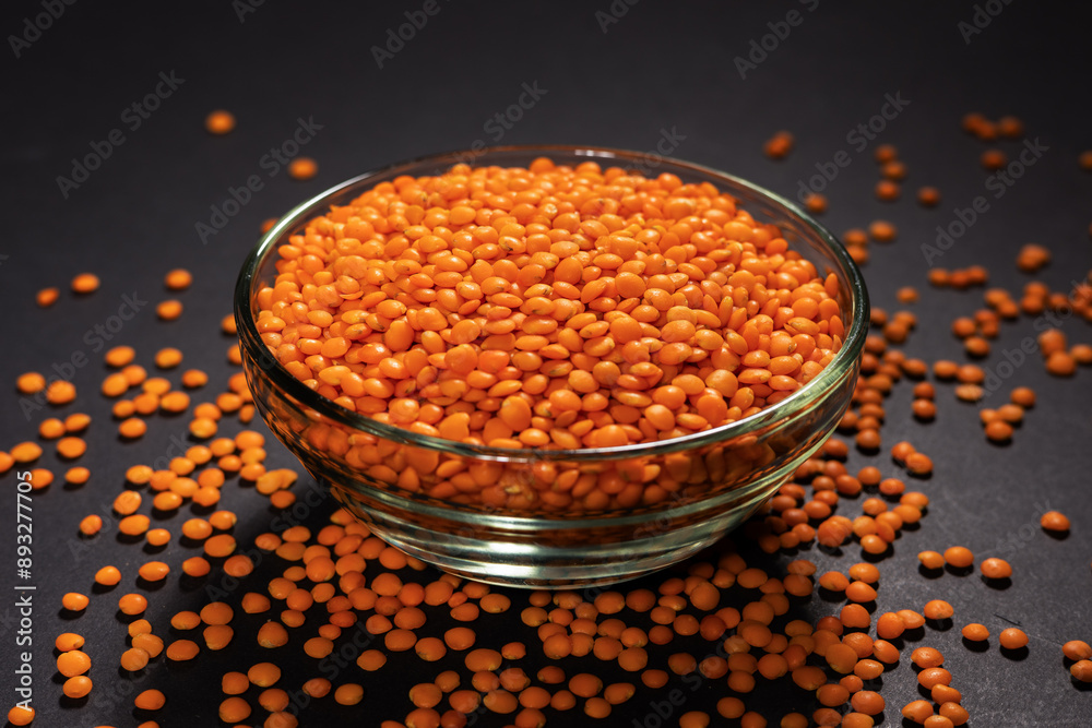 Red lentils in glass plate on dark background Red lentils in glass plate on dark background