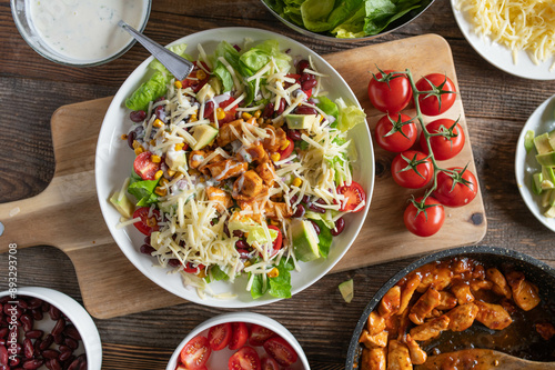 Tex mex barbecue chicken salad with kidney beans, avocado, cheese, lettuce, tomatoes, corn and ranch dressing on a plate