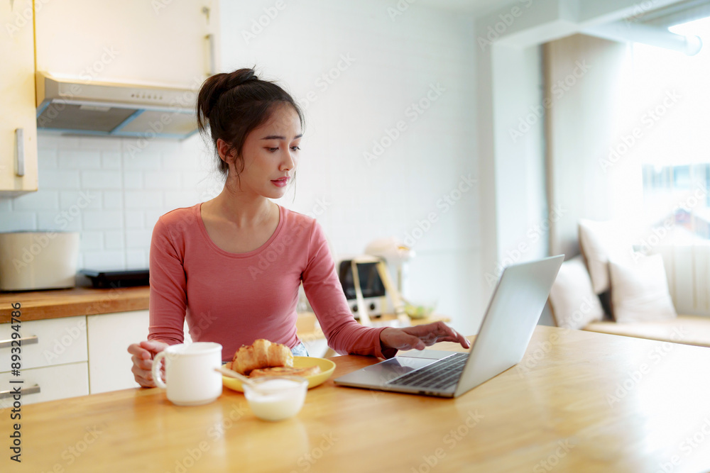 Asian girl having breakfast on sofa using laptop at home in the morning Asian girl having breakfast on sofa using laptop at home in the morning