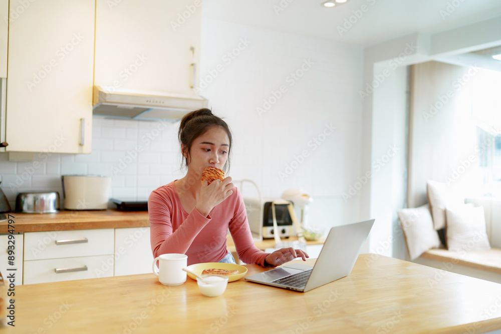 Asian girl having breakfast on sofa using laptop at home in the morning Asian girl having breakfast on sofa using laptop at home in the morning