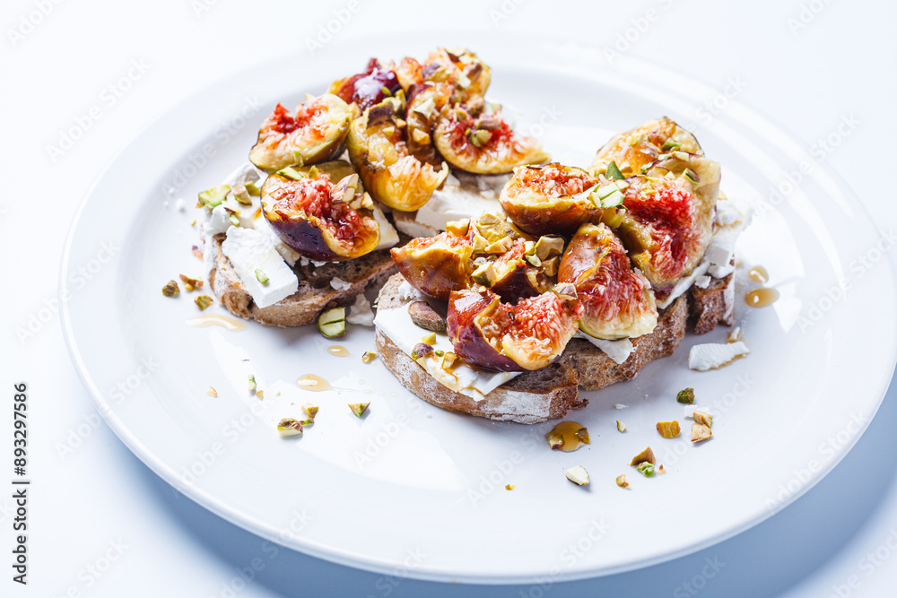 Breakfast toast with feta cheese, figs and pistachios on white plate, white background. Breakfast toast with feta cheese, figs and pistachios on white plate, white background.