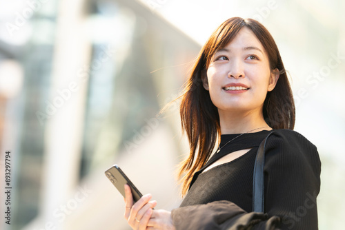 駅前でスマホを持って笑っている女性
