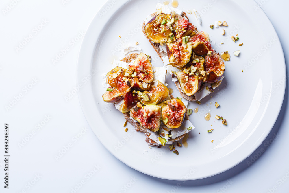 Breakfast toast with feta cheese, figs and pistachios on white plate, white background. Breakfast toast with feta cheese, figs and pistachios on white plate, white background.