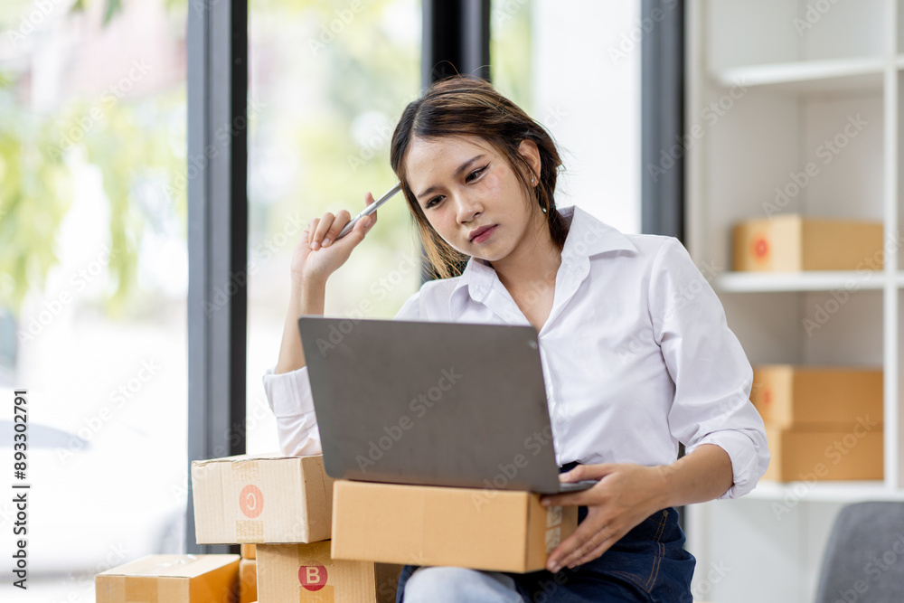 Portrait business woman smile and use laptop checking information on parcel shipping box before send to customer. Entrepreneur small business working at home. SME business online marketing. Portrait business woman smile and use laptop checking information on parcel shipping box before send to customer. Entrepreneur small business working at home. SME business online marketing.