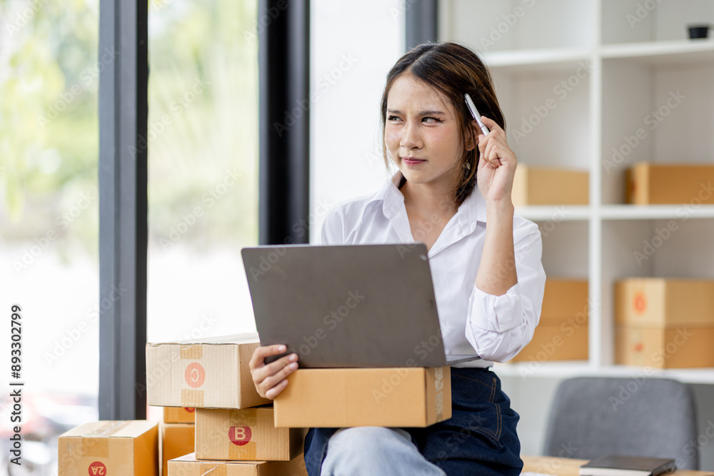Portrait business woman smile and use laptop checking information on parcel shipping box before send to customer. Entrepreneur small business working at home. SME business online marketing. Portrait business woman smile and use laptop checking information on parcel shipping box before send to customer. Entrepreneur small business working at home. SME business online marketing.