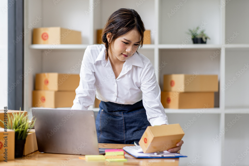 SME concept. Young asian female ecommerce business owner prepares package box for customer and delivery check balance.  SME small business entrepreneur SME or freelance