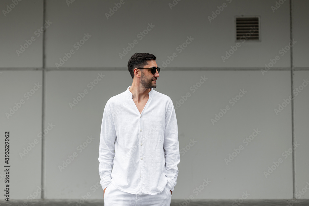 Fashion cool business man with sunglasses in white shirt walks in the city near a gray wall Fashion cool business man with sunglasses in white shirt walks in the city near a gray wall