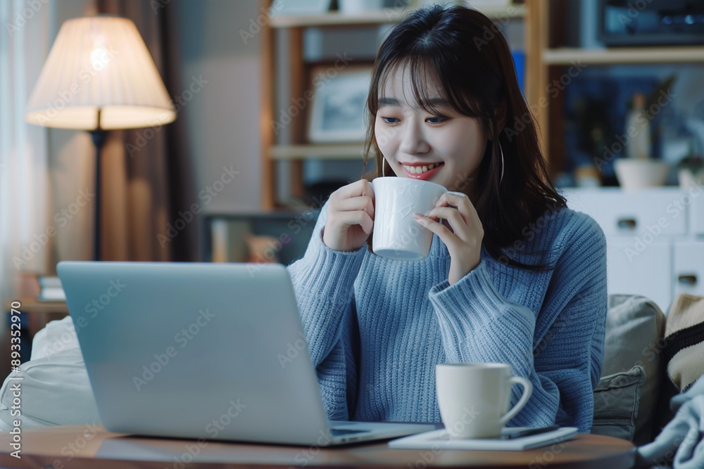 Freelancer asian woman working from home and using laptop sitting in living room with cup of hot coffee enjoying Freelancer asian woman working from home and using laptop sitting in living room with cup of hot coffee enjoying