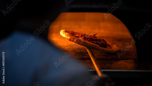 A professional chef maneuvers a pizza onto stone inside a wood fired oven.