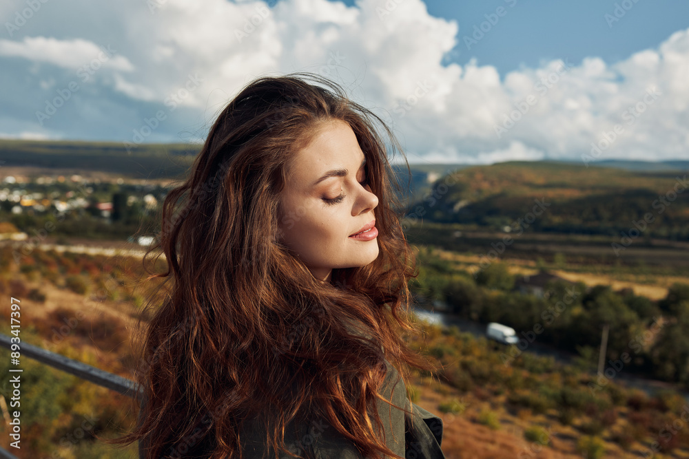 Beautiful young woman with long hair standing on a hillside enjoying the breathtaking view of the countryside landscape