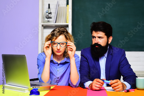 Serious male and female teachers sitting at desk in classroom. Students couple on test or exam in university campus. High school, learning and education. Couple of teachers man and woman at college.