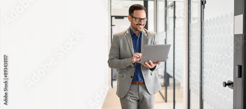 Portrait of happy young male professional working on project over wireless computer in office corridor