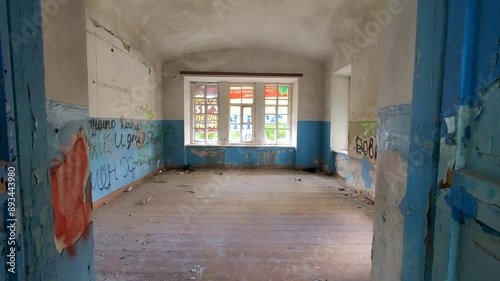 Dilapidated classroom inside old school, revealing peeling blue and white paint, graffiti, inscriptions and dust-covered floors. Halloween or horror interior