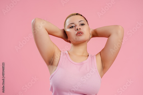 Confident queer woman posing with hands on head on pink background © Maria Vitkovska