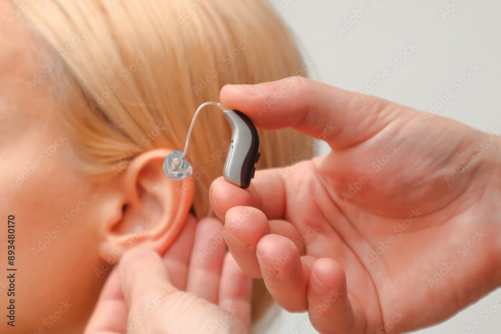 Fototapeta premium Doctor putting an hearing aid. The hands of a male audiologist trying on a hearing aid on a woman's ear. Helping technologies for people with disabilities