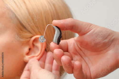 Doctor putting an hearing aid. The hands of a male audiologist trying on a hearing aid on a woman's ear. Helping technologies for people with disabilities photo