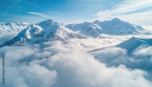 An aerial view captures a snowy mountain range enveloped by clouds under a vast sky