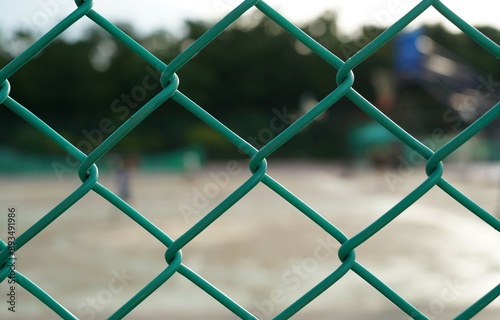 Close up a green net fence of the sports stadium back side blur people playing sports.