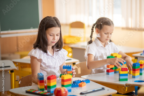 Cute girls sit in the classroom at a desk and build a building from blocks of bright construction materials during the lesson. Back to school. School supplies. Student at a lesson 