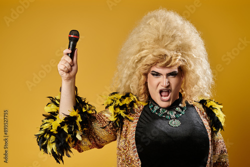 A drag queen in a glamorous outfit and a large blonde wig sings into a microphone. photo