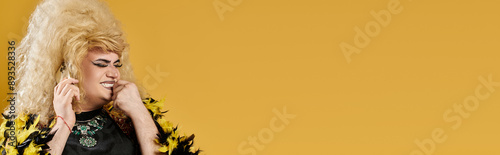 A drag queen in a yellow feathered jacket smiles against a bright yellow backdrop. photo