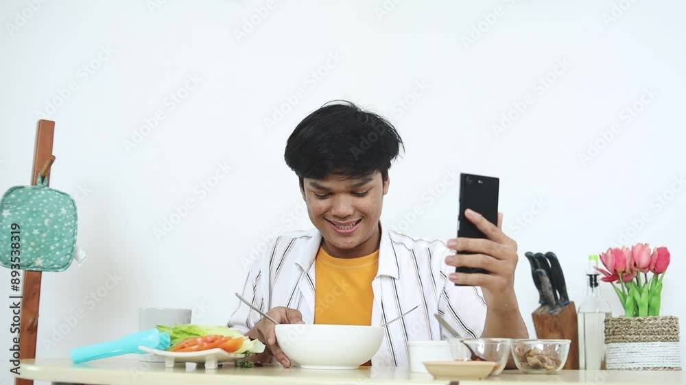 Asian Young Man Eating And Showing Noodle To Camera While Recording Food Content Video By Using Smartphone Asian Young Man Eating And Showing Noodle To Camera While Recording Food Content Video By Using Smartphone
