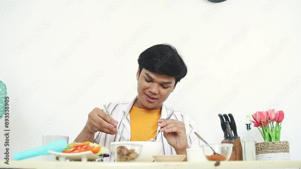 Asian Young Man Sitting In The Kitchen Table And Enjoying Eating Homemade Noodle Asian Young Man Sitting In The Kitchen Table And Enjoying Eating Homemade Noodle