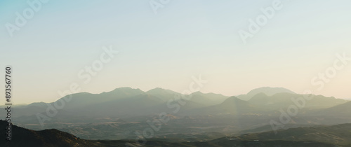 Panoramic view of serene mountain range at sunrise with mist and soft light