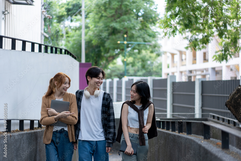 Three young people are walking down a sidewalk, one of whom is holding a tablet Three young people are walking down a sidewalk, one of whom is holding a tablet